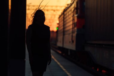 Tren peronu gün batımında. Gün batımında güneşin güzel altın ışığı. Trenle yolculuk zamanı. Kız sırtı dönük istasyonda duruyor ve trenin gelişini bekliyor.