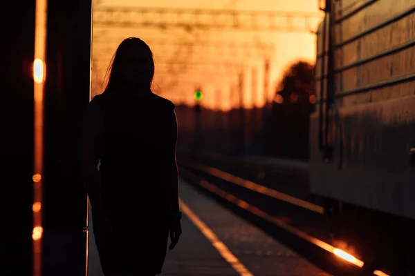 Tren peronu gün batımında. Gün batımında güneşin güzel altın ışığı. Trenle yolculuk zamanı. Kız sırtı dönük istasyonda duruyor ve trenin gelişini bekliyor.