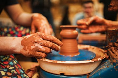 Bir çömlekçi ve bir öğrenci çömlekçi çarkında kilden yapılmış tabaklar yapıyorlar.