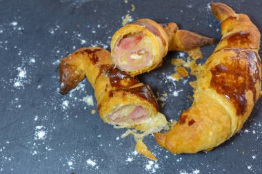 Jambon ve erimiş peynirle doldurulmuş taze pişmiş kruvasanlar, yemeye hazır, gri bir tabakta.