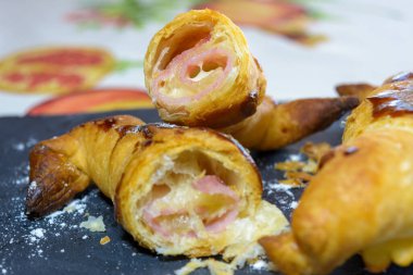 Jambon ve erimiş peynirle doldurulmuş taze pişmiş kruvasanlar, yemeye hazır, gri bir tabakta.