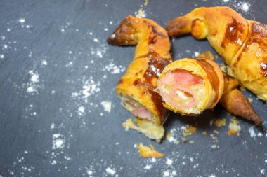 Jambon ve erimiş peynirle doldurulmuş taze pişmiş kruvasanlar, yemeye hazır, gri bir tabakta.