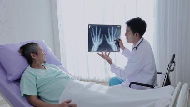 亚洲男性医生手握手部骨片与男性病人交谈 解释治疗方法 并给予鼓励 — 图库视频影像