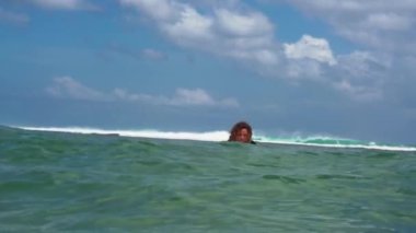 Mavi okyanustaki beyaz sörf tahtasındaki sörfçü kızın Bali 'deki sudan çekilmiş görüntüleri.