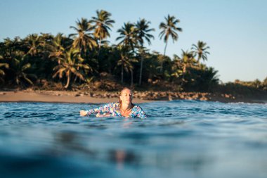 Dominik Cumhuriyeti 'nin Encuentro sahilinde mavi okyanusta beyaz sörf tahtasındaki sarışın sörfçü kızın portresi.
