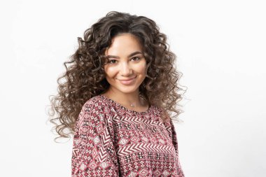 Kıvırcık, uzun siyah saçlı, kıvırcık saçlı güzel bir kadın model saç maşasında gülümser ve beyaz arka planda bir portre için poz verir..