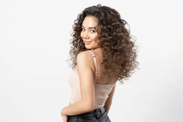 Kıvırcık, uzun siyah saçlı, kıvırcık saçlı güzel bir kadın model saç maşasında gülümser ve beyaz arka planda bir portre için poz verir..