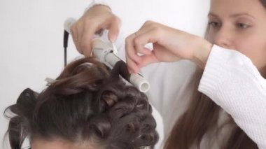 Saç stilisti, uzun siyah saçlı güzel bir kız için saç stili yapar.