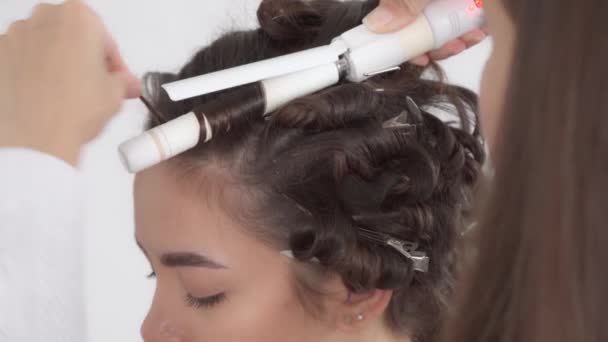 Um cabeleireiro faz um penteado para uma menina bonita jovem com cabelo escuro longo — Vídeo de Stock