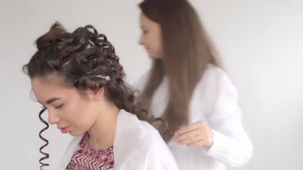 Un parrucchiere fa un'acconciatura per una giovane bella ragazza con lunghi capelli scuri — Video Stock