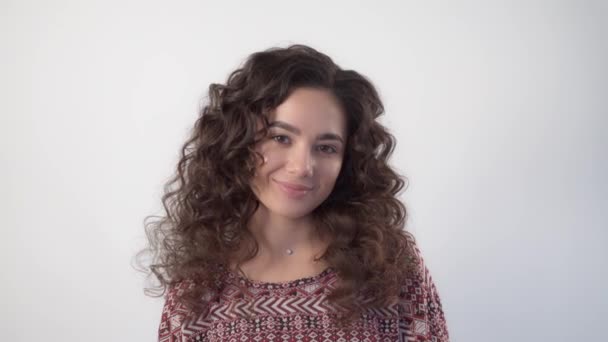 En ung kvinna med långt lockigt hår tittar på kameran med ett lätt leende — Stockvideo