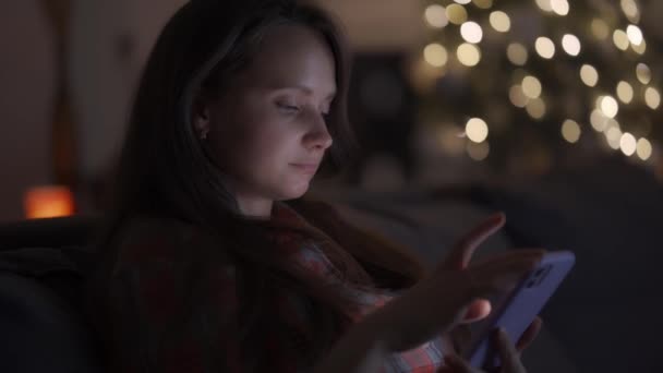 Uma mulher solitária em casa tarde da noite, olhando para a tela do smartphone e entediada — Vídeo de Stock