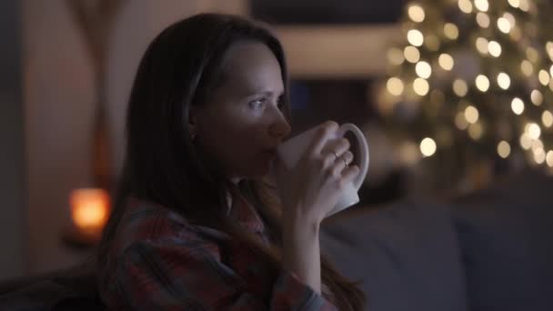 A woman drinks hot tea or coffee and watches movies or news on TV — Stock Video
