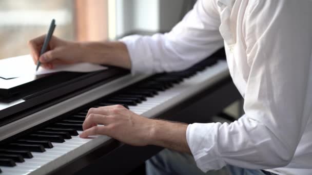 The composer plays the piano composes music and writes it down with notes — Stock Video