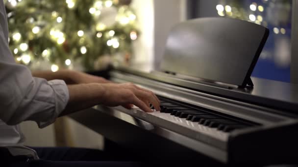 En pianistisk musiker spelar ett digitalt piano bredvid en julgran — Stockvideo