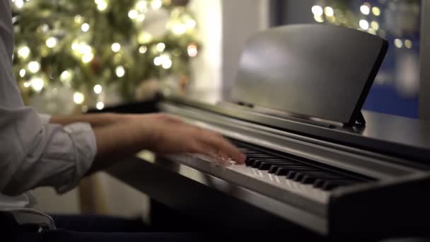 Пианист играет на цифровом пианино рядом с елкой — стоковое видео