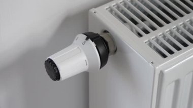 Bir kadın termostatı çevirerek radyatör sıcaklığını düşürür.