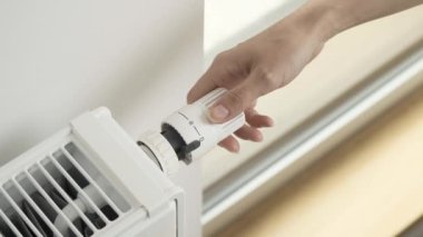 Kadın odadaki ısıtıcının sıcaklığını maksimuma çıkarmak için radyatörün termostatik valfinin regülatörünü çeviriyor. Soğuk havada dairenin ısıtılması ve şiddetli dondurmalar.