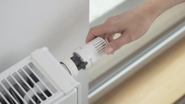 Kadın odadaki ısıtıcının sıcaklığını maksimuma çıkarmak için radyatörün termostatik valfinin regülatörünü çeviriyor. Soğuk havada dairenin ısıtılması ve şiddetli dondurmalar.