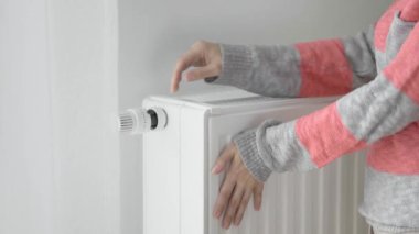Bir kadın soğuk ısıtıcının ısıtıcısına donmuş elleriyle dokunur ve ısıtma gücünü maksimum değerle arttırır. Isınma mevsiminde enerji tüketimini sınırlıyor. Enerji krizi..