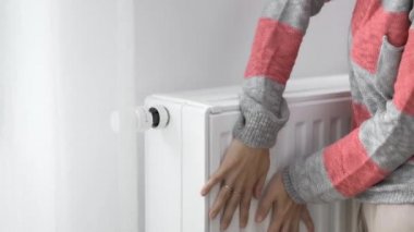 Bir kadın soğuk ısıtıcının ısıtıcısına donmuş elleriyle dokunur ve ısıtma gücünü maksimum değerle arttırır. Isınma mevsiminde enerji tüketimini sınırlıyor. Enerji krizi..
