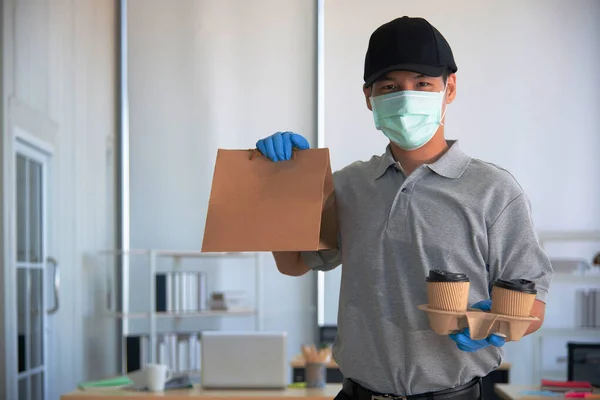 Eldiven takan ve cerrahi maske takan bir teslimatçı müşteriye bir fincan sıcak kahve veriyor.