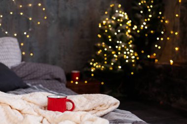 Sıcak kış arka planında bir yatak ve arka planda bir Noel ağacı olan bir fincan.