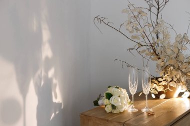 Alyanslar iki kadeh şampanya ve güneşte bir buket gülün yanında.