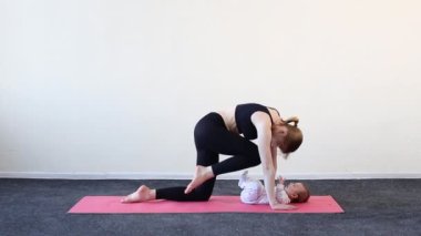 Genç anne evde bebekle yoga yapıyor.