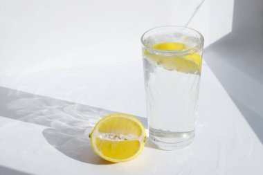Beyaz, güneşli arka planda limonlu bir bardak su.