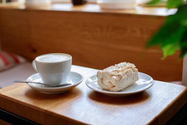 Bir fincan taze kapuçino ve kahve dükkanındaki masanın üstünde kremalı pasta. yakın plan