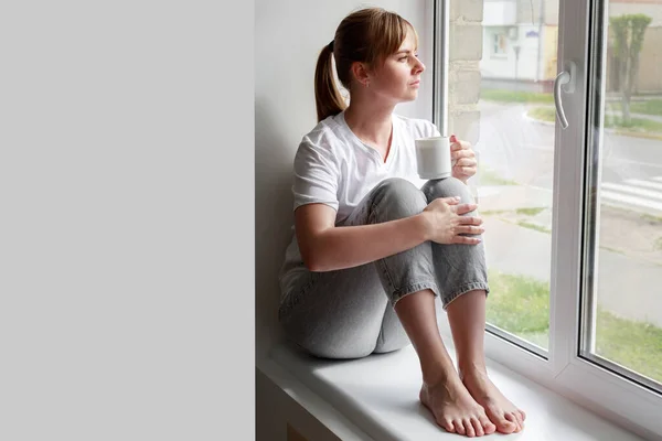 a woman with a cup of tea sits on the window. free space for text