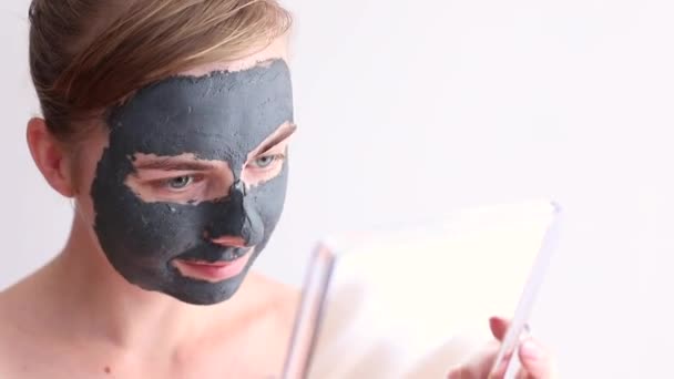 Kobieta Czarnej Glinianej Masce Kosmetycznej Spogląda Lustro Zabiegi Kosmetyczne Domu — Wideo stockowe