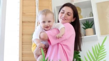 Anne, evde oynarken kollarında bir bebekle pencerenin yanında oynuyor. Çocukların boş vakitleri. çocuk gelişimi, aile