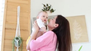 Anne, kollarında bebekle evdeki pencerenin yanında oynuyor..