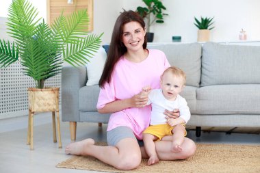 Anne ve bebek oturma odasında birlikte gülümsüyor.