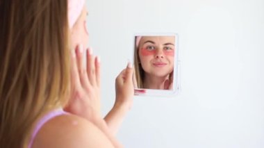 a woman in patches under her eyes looks in the mirror. cosmetic care
