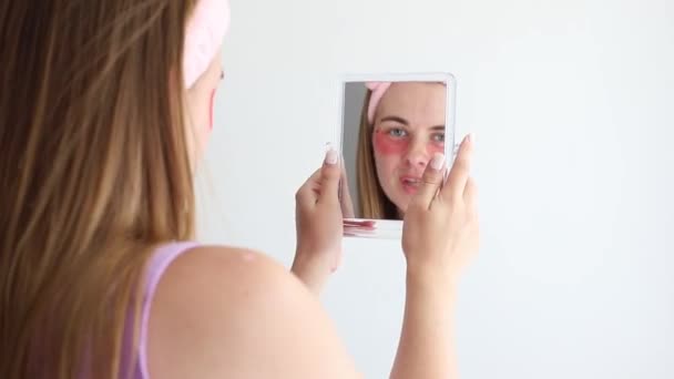 Μια Γυναίκα Μπαλώματα Κοιτά Στον Καθρέφτη Γκρι Φόντο Περιποίηση Προσώπου — Αρχείο Βίντεο