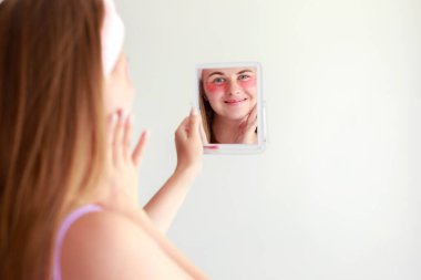 woman in patches under her eyes looks in the mirror