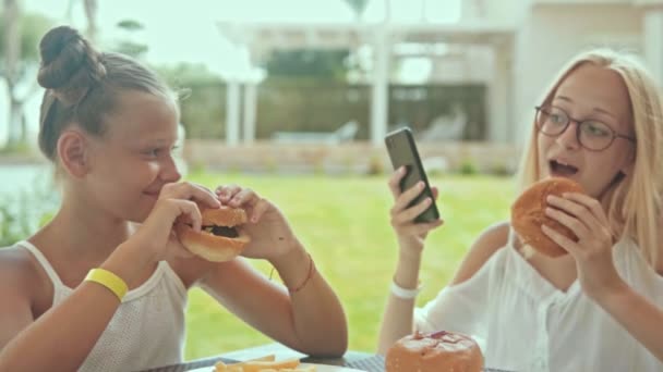 Two Teen Girlfriends Eating Burgers Taking Selfies Laughing — Video