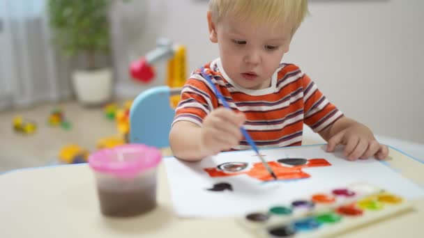 一个金发碧眼的小男孩坐在桌旁，画了一辆涂有颜料的汽车 — 图库视频影像