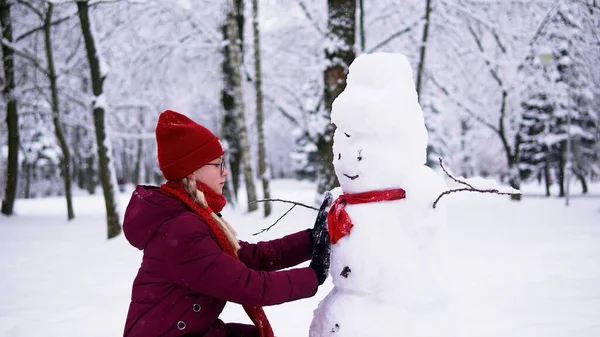 Girl Red Jacket Makes Snowman Snowy Forest Knits Red Scarf — Zdjęcie stockowe