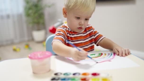 Мальчик Светлыми Волосами Сидит Столом Рисует Радугу Красками Бумаге — стоковое видео
