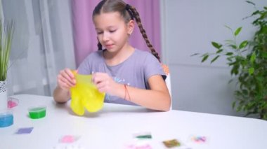 Genç kız evdeki masada yeşil parlak sümükle oynuyor.