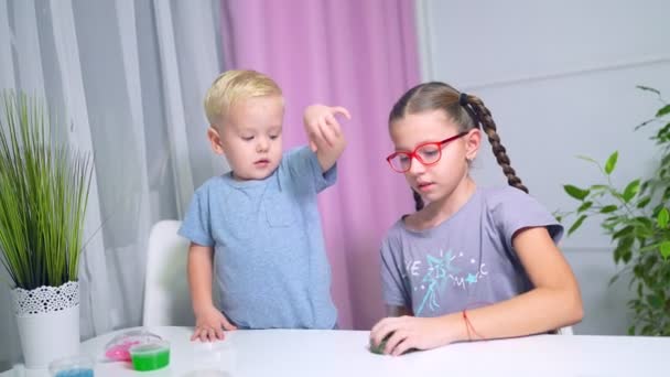 Jongen en meisje spelen met groen glanzend slijm aan de tafel thuis. — Stockvideo