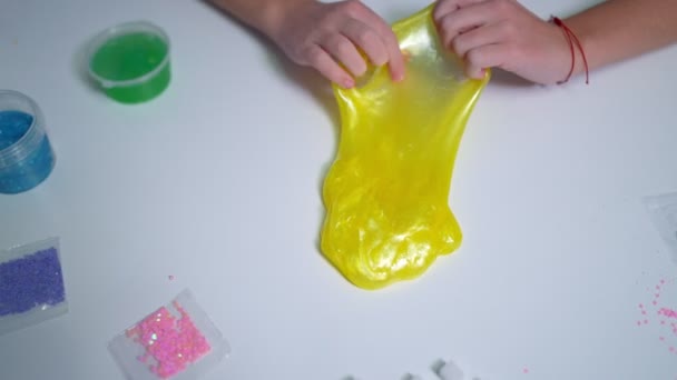 Dívky ruka hraje se žlutým lesklým slizem u stolu doma — Stock video