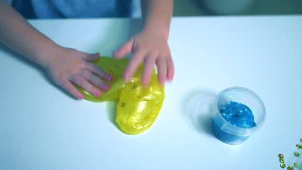 Little boy blond playing with yellow shiny slime at the table at home — Stockvideo