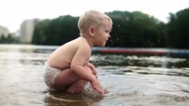 Sarı saçlı çocuk suda duruyor ve göle sıçrıyor. Su sıçraması