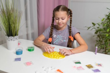 Genç kız evdeki masada yeşil parlak sümükle oynuyor..