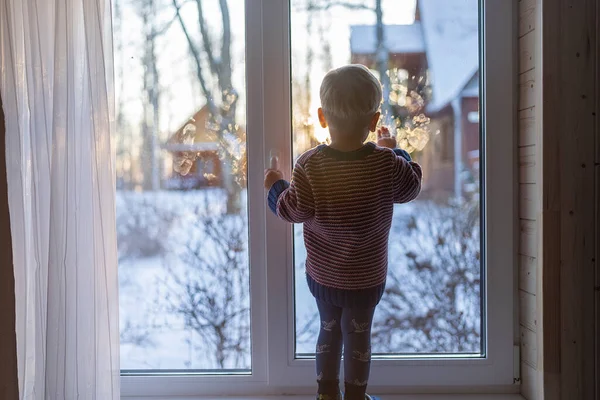 stock image little boy stand near the window and look at the snowy street in winter, when it is very cold.